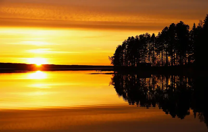 Un coucher de soleil sur un lac finlandais, avec un chalet d'été caché dans les arbres d'un petit cap, en juin 2026.