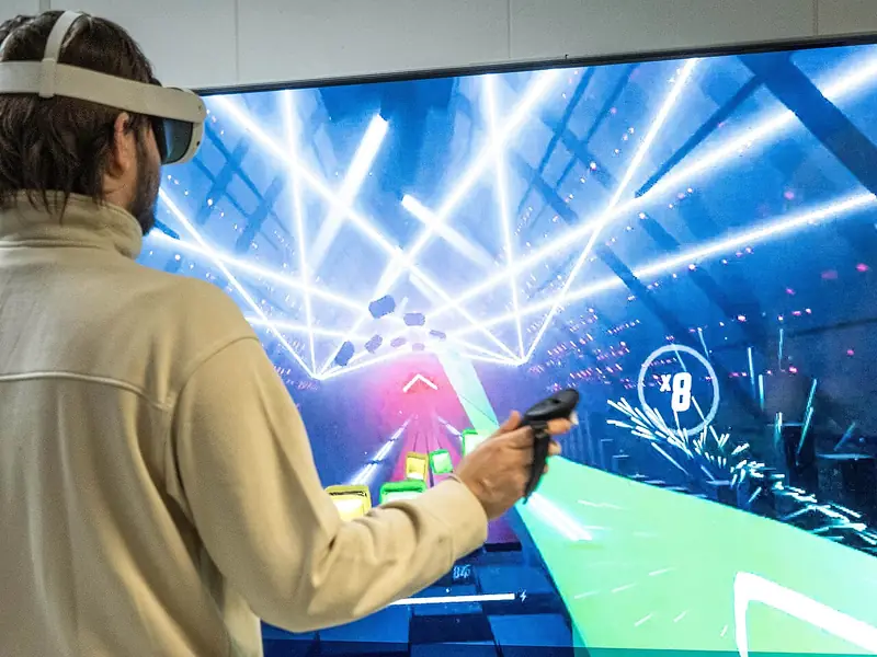 Un joueur, casque de réalité virtuelle sur la tête et manette en main, dans une partie de Beat Saber affichée sur grand écran.